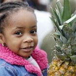 Young girl standing with a pineapple and learning about healthy food choices as part of the Food for Kids program managed by the Community Food Bank of Eastern Oklahoma.
